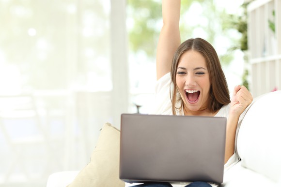 A lady celebrates good news on her laptop at home.
