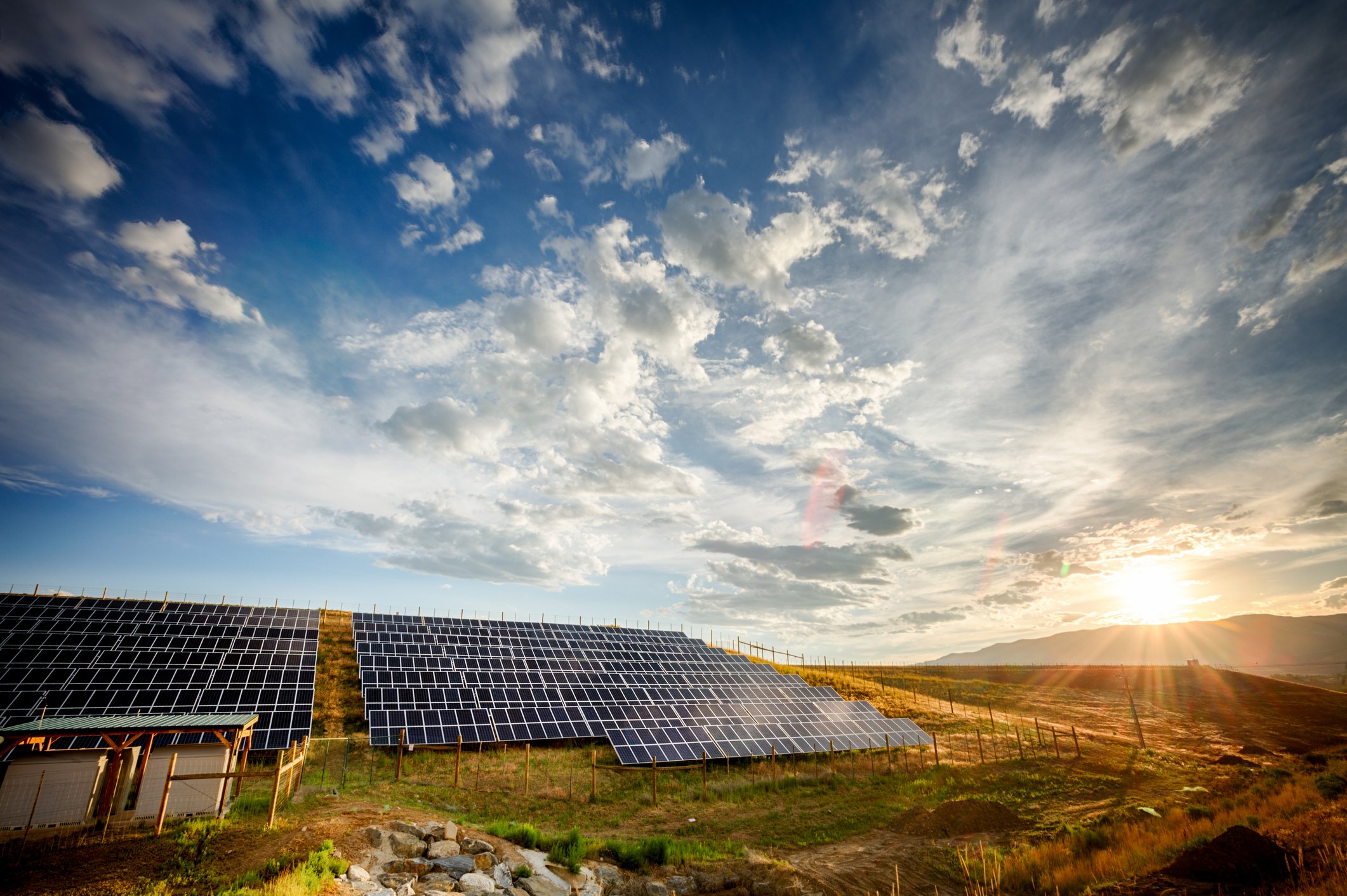 A solar farm with a bright sun in the background.
