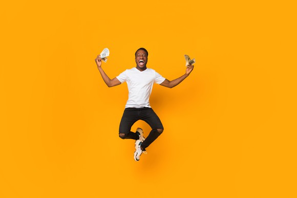 Excited man jumping while holding cash in hand
