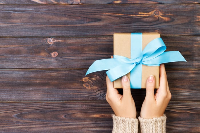 Hands holding small box with blue ribbon on a wood table.