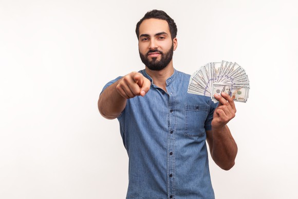 A man holding bills fanned out in one hand and pointing straight ahead with the other.