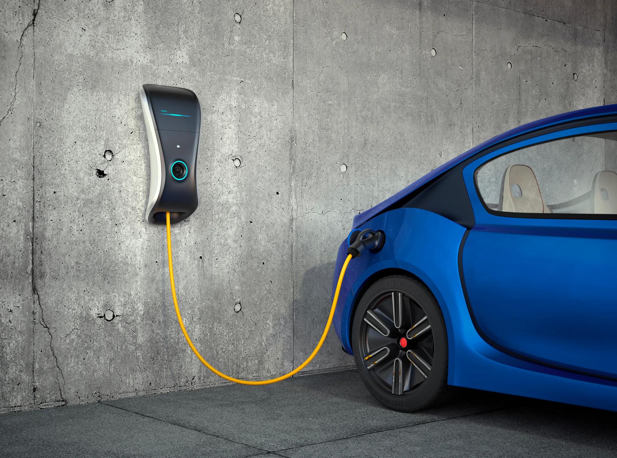 Blue car plugged into a charger on a concrete wall.