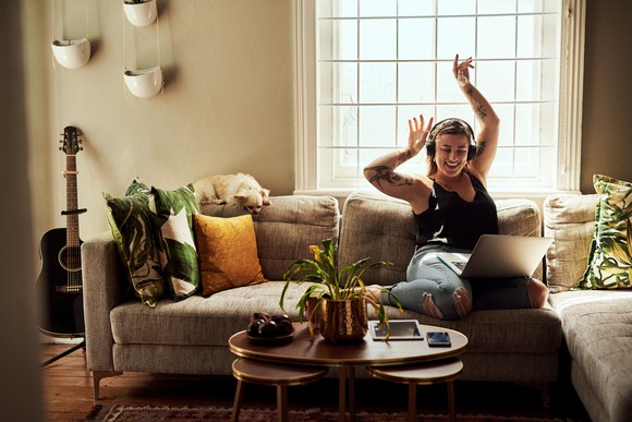 Woman listening to headphones on her couch and raising her arms