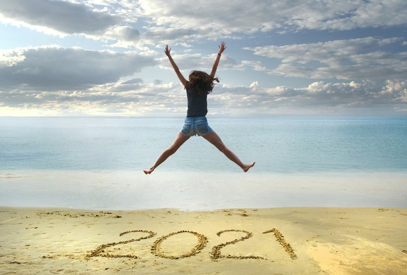 Someone jumping high over a 2021 scrawled on beach sand.