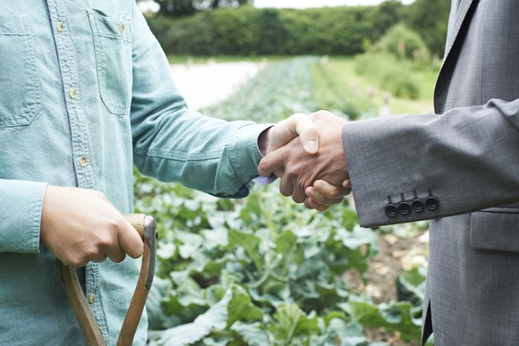 Close-up of a farmer and a banker shaking hands in a field.