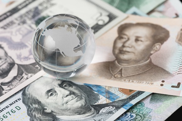 Paper currency from the U.S. and China, with a small shiny globe as a paperweight
