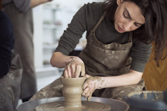 Woman molding clay into an object on a potter's wheel.