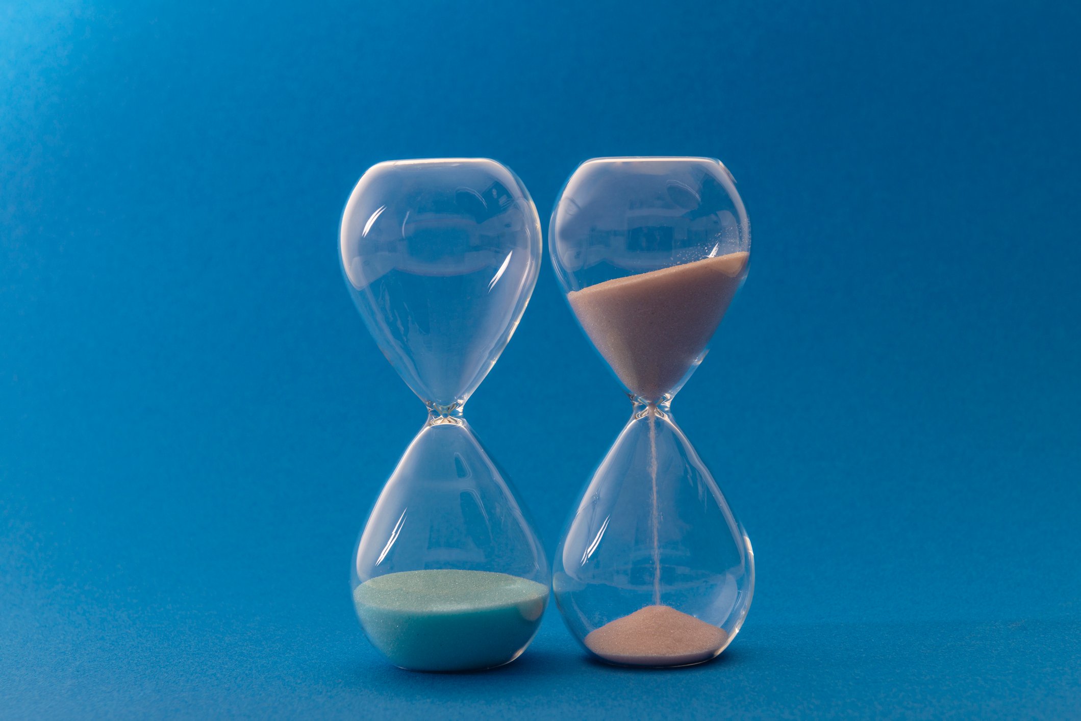 An hourglass with all of its sand at the bottom next to another hourglass with most of the sand still in the top half