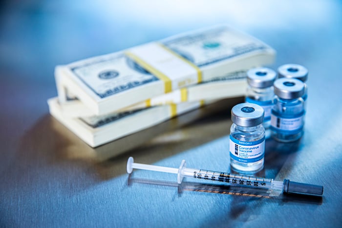 COVID-19 vaccine vials next to a syringe and stacks of cash