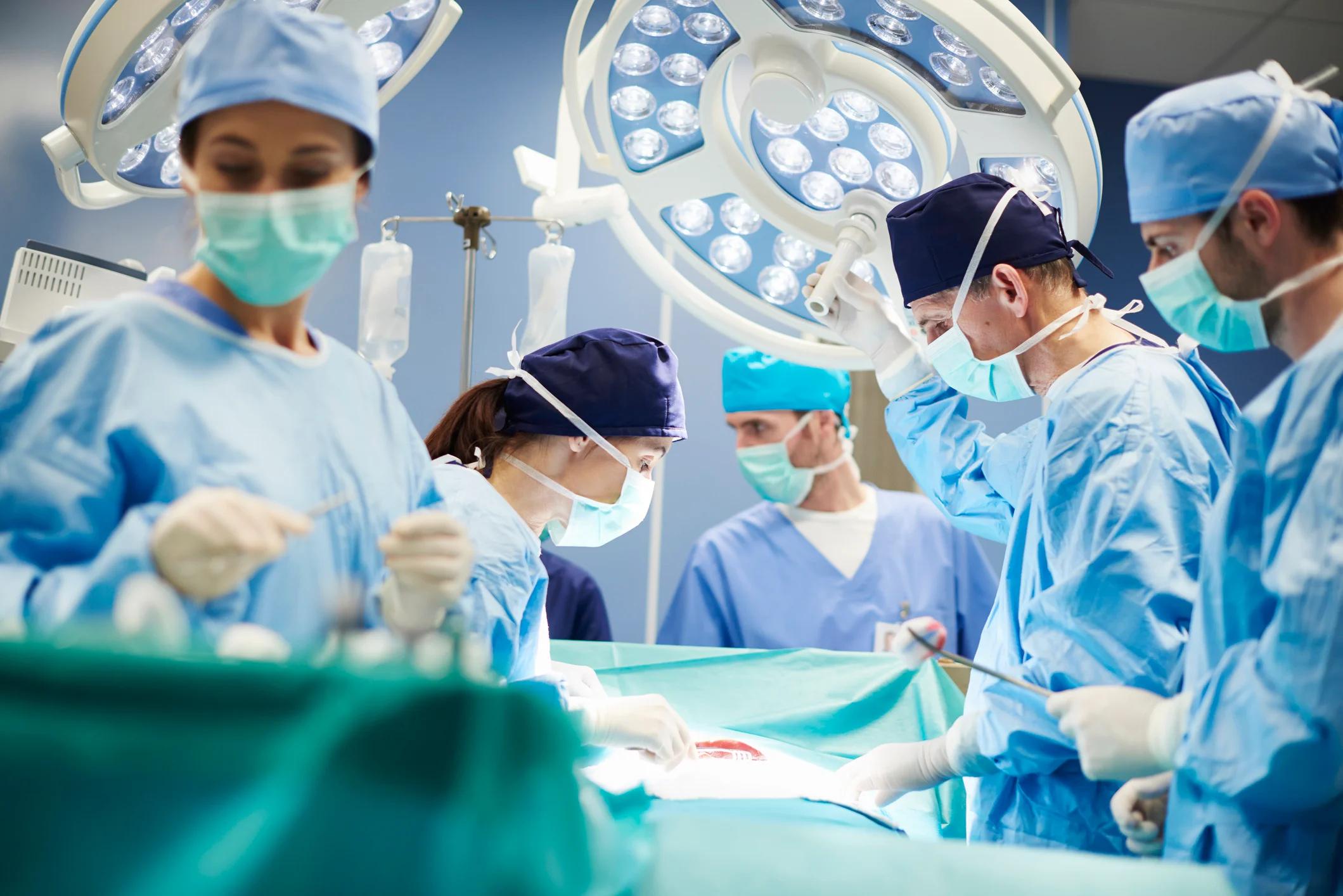 Several medical professionals wearing masks and scrubs in surgery with a patient.