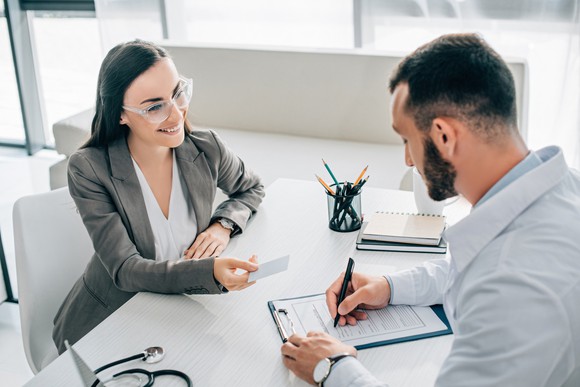 Man and woman sitting at a desk with the man filling out paperwork.