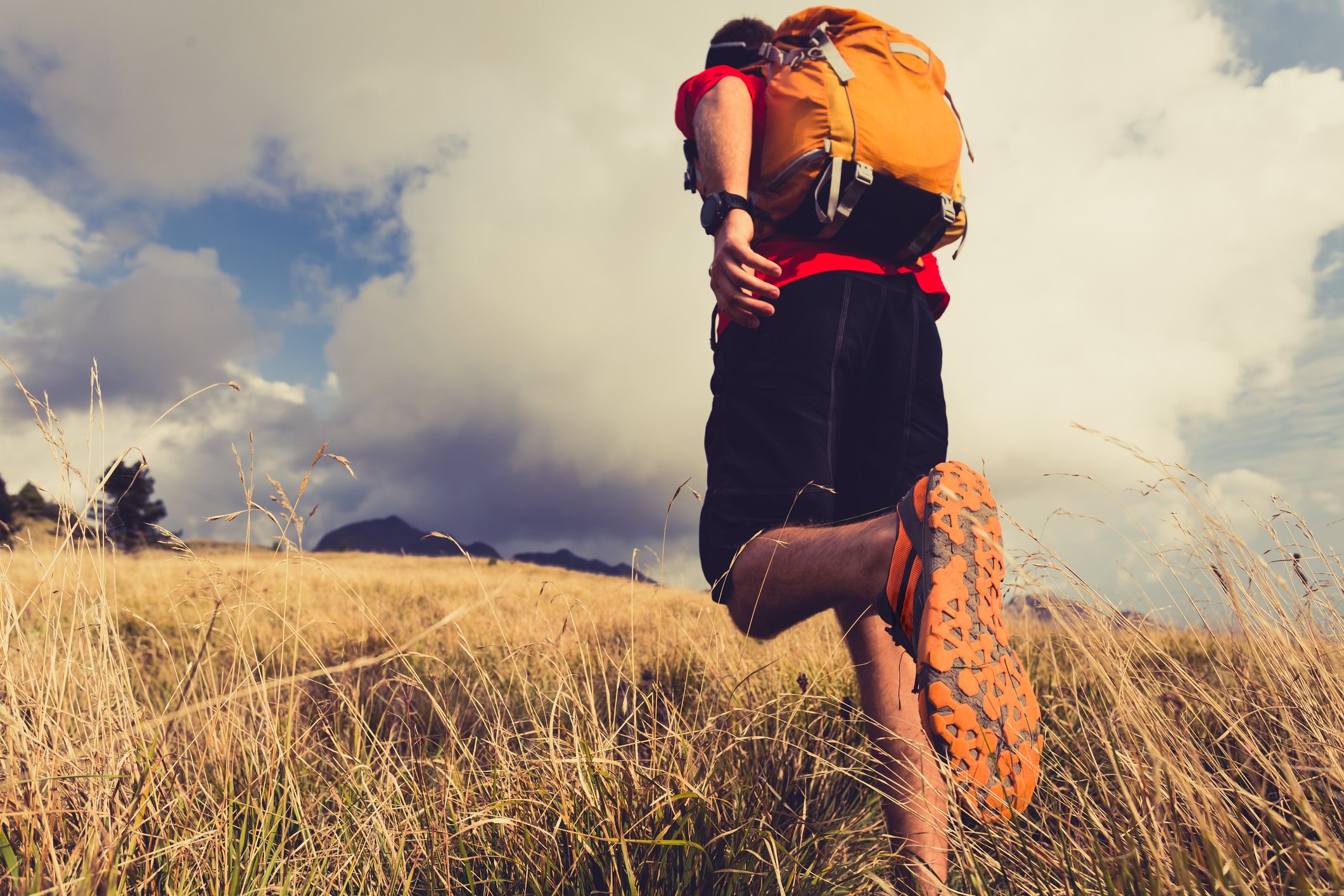 An outdoor enthusiast wearing a backpack runs in a field.