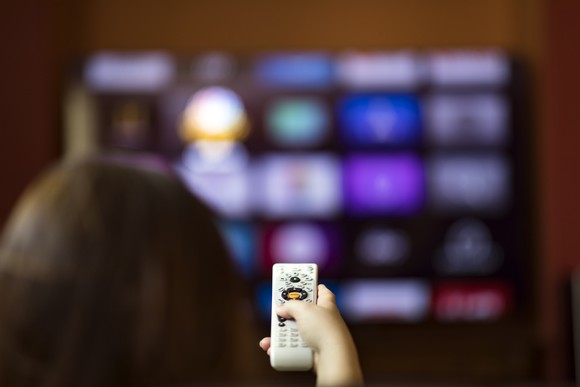 A person points a remote control at a TV.