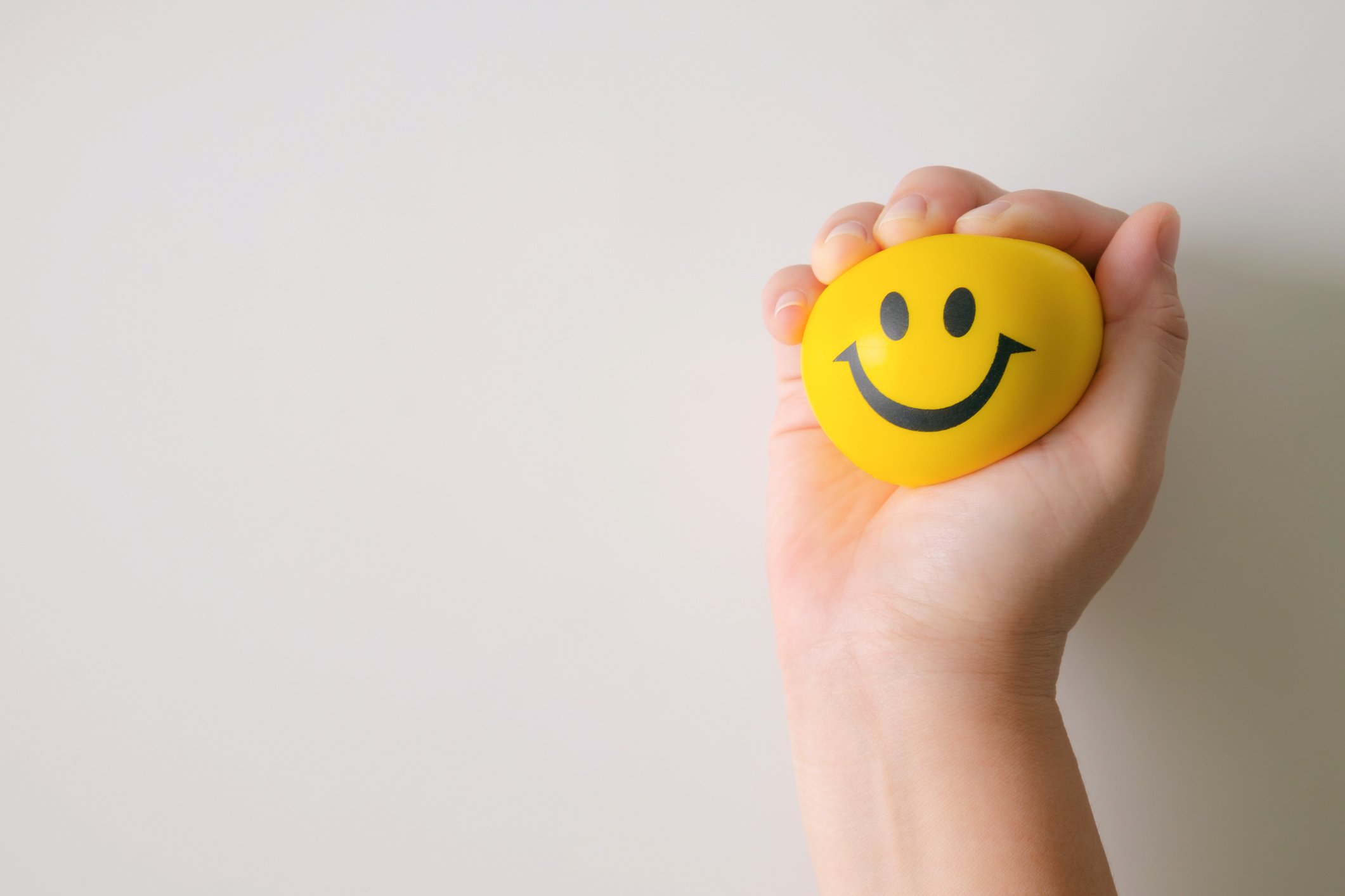 A hand squeezes a yellow, smiley-face stress ball.