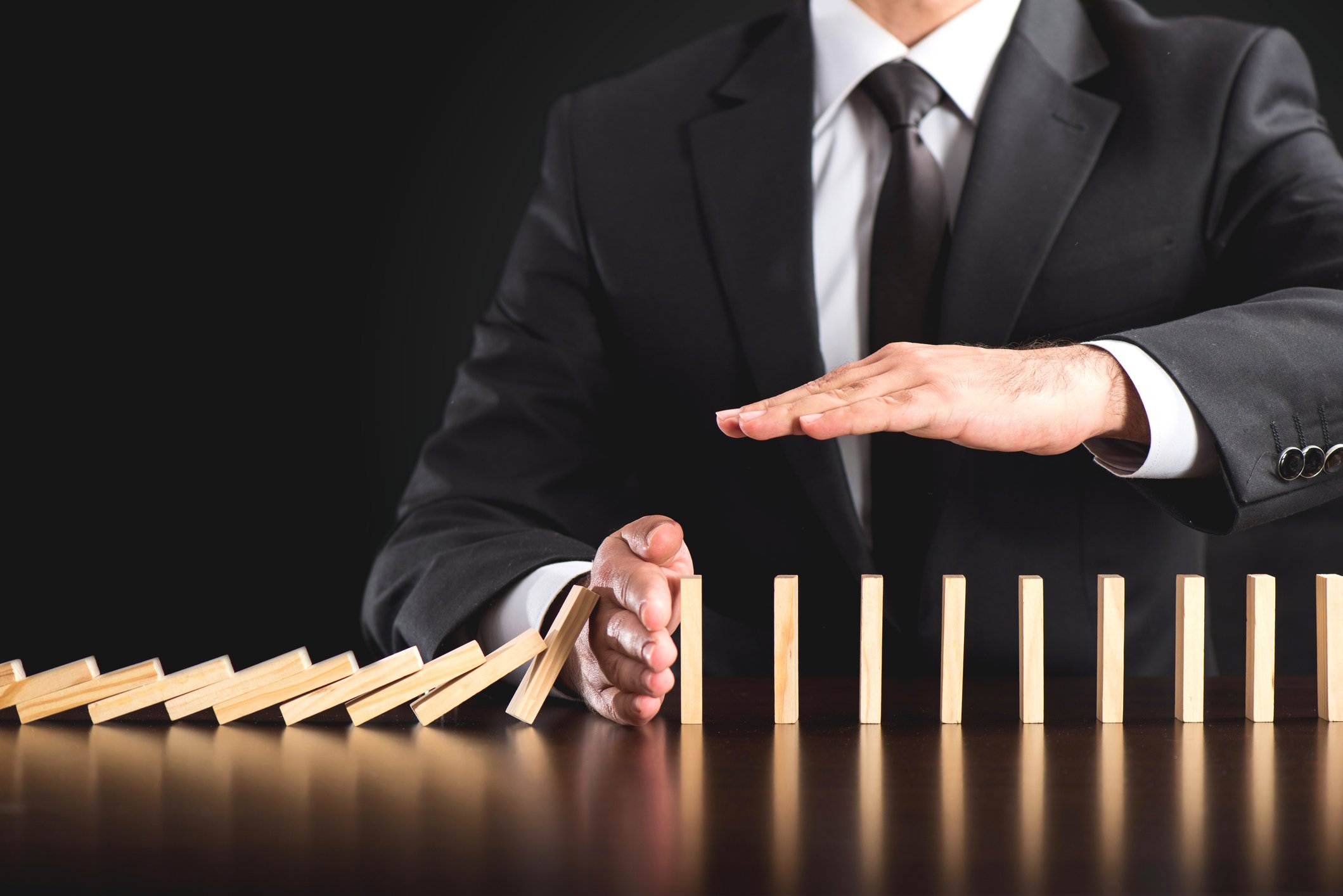 A man in a business suit stopping a row of dominoes from falling over.
