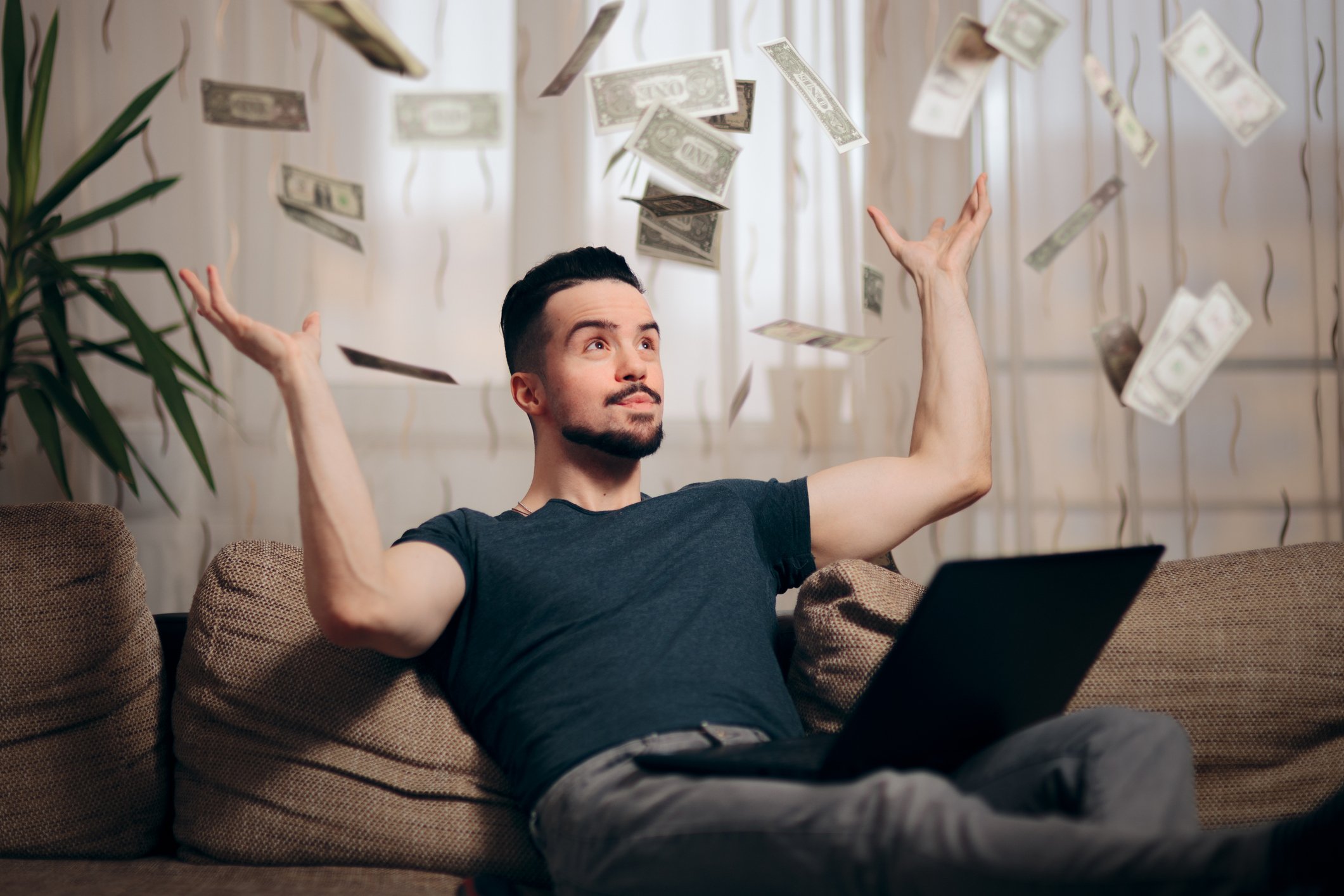 Man sitting on couch with laptop as money rains down