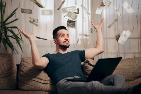 Man sitting on couch with laptop as money rains down