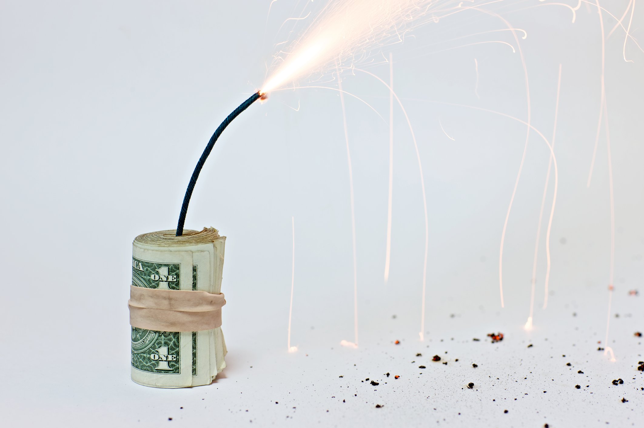 A roll of dollar bills, wrapped in a rubber band, with a lit fuse sticking out of it.