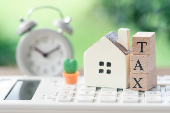 A model house is placed on the wooden word TAX.