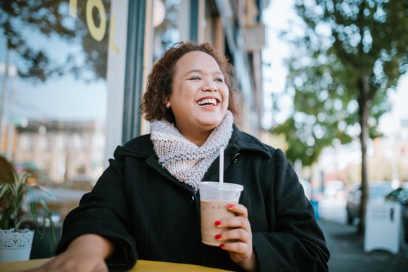 Smiling woman holding coffee beverage outside a coffee shop