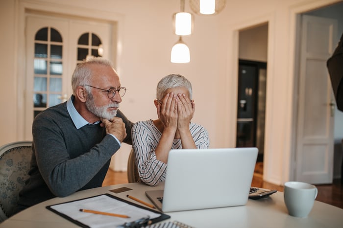 Older couple looking at their laptops in dismay.