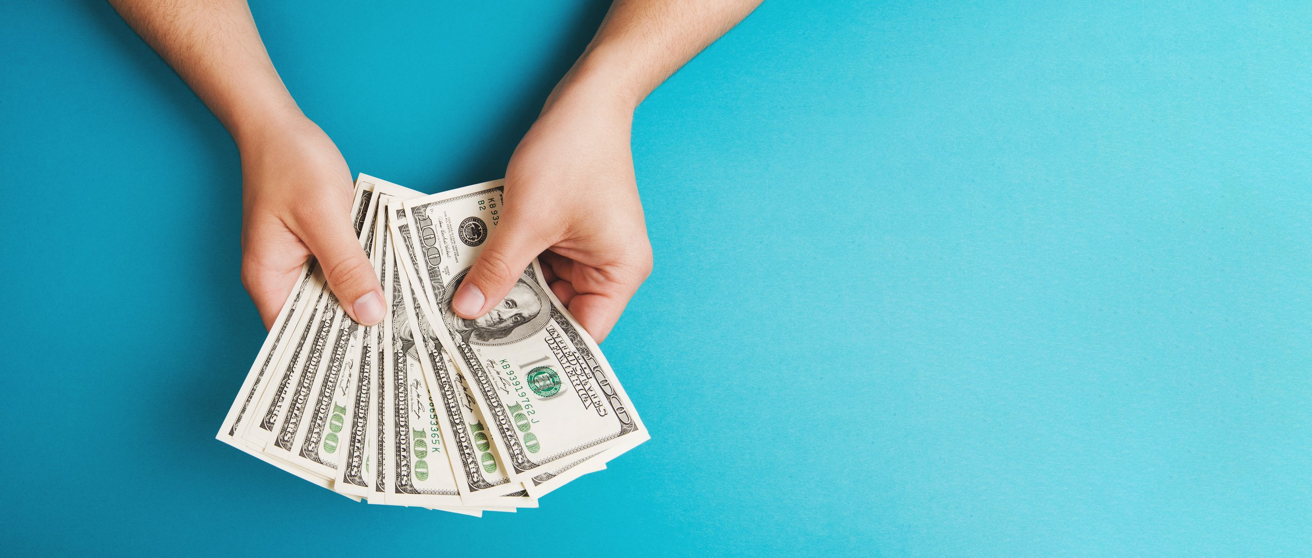 A man holds fanned out one hundred dollar bills.