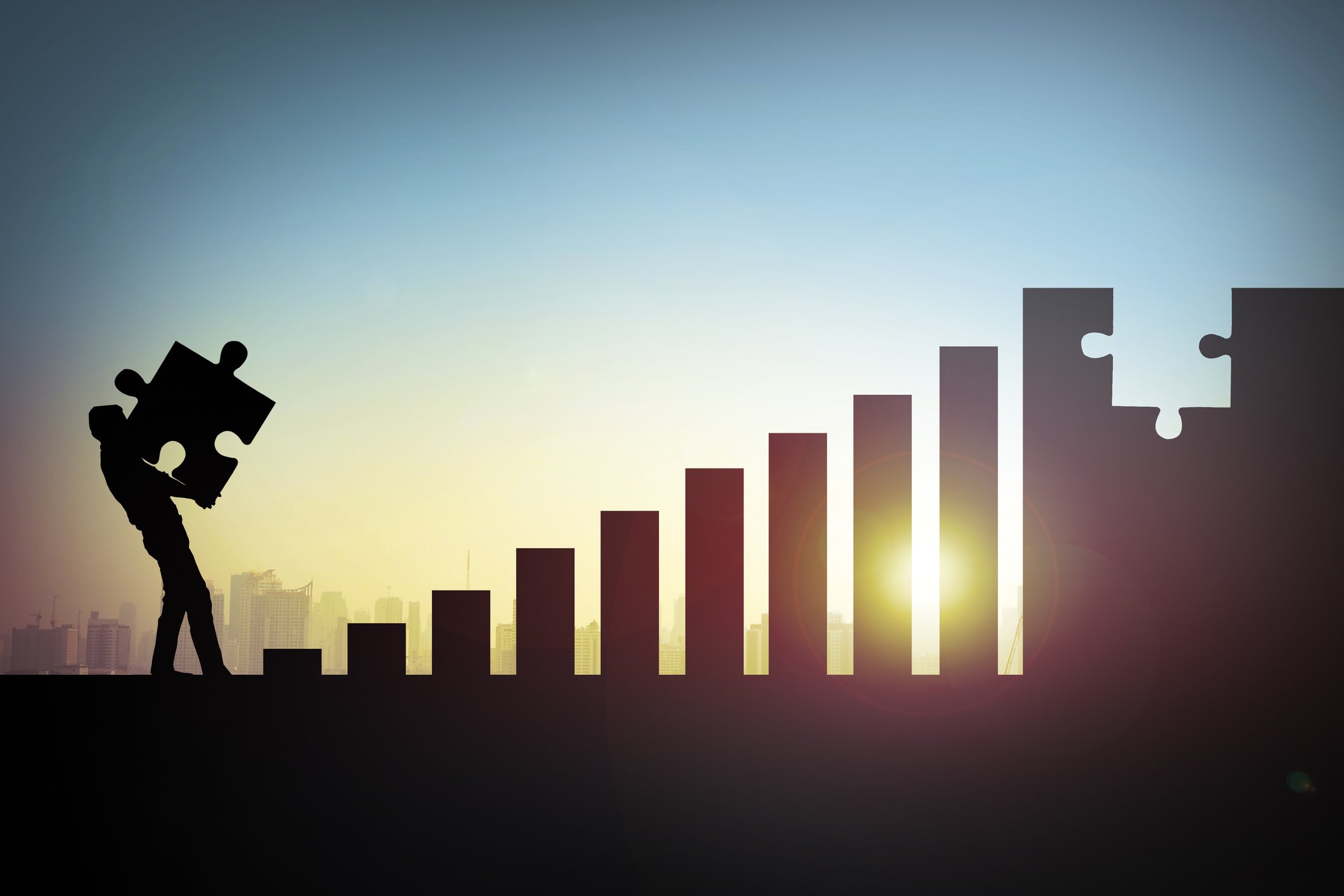 An ascending bar chart missing a puzzle piece and a person holding the piece. 