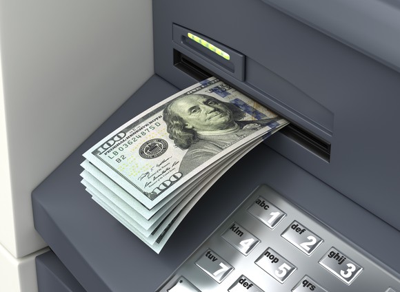 An ATM is spitting out a bunch of hundred-dollar bills. 