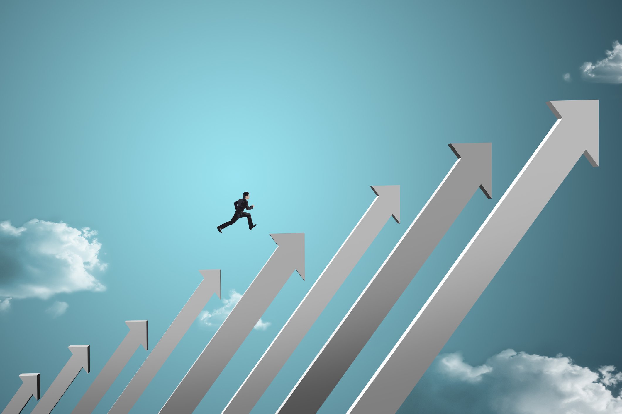 businessman running over arrows pointing upward and increasing at an angle against backdrop of blue sky