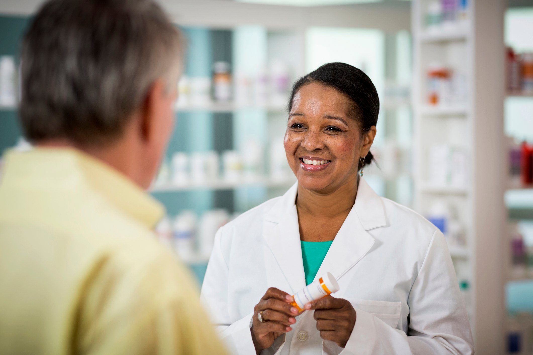 A smiling pharmacist holding a prescription bottle and consulting with a patient. 