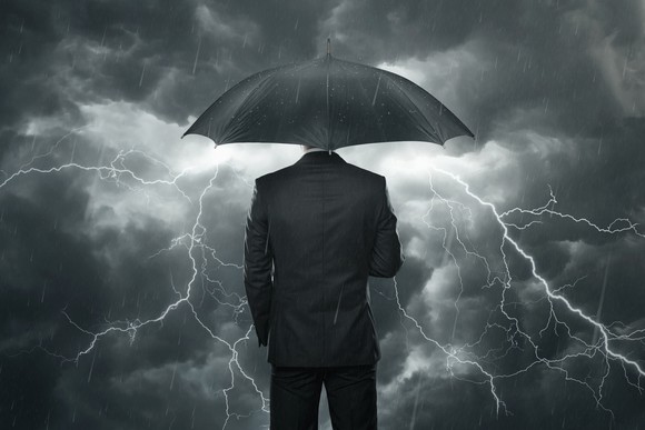 A businessman stands under his umbrella, watching the rain and thunderclouds around him.
