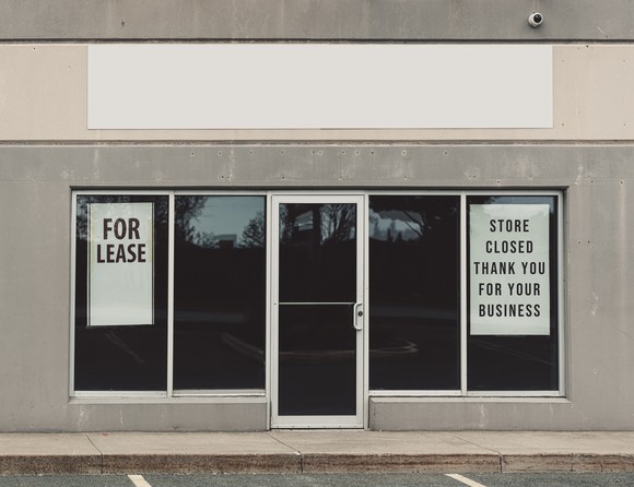 A storefront with a For Lease sign and a sign saying the store is closed.