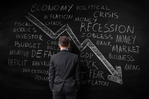 A man stares at a chalkboard with many reasons the stock market would fall and a large arrow pointed down and to the right.