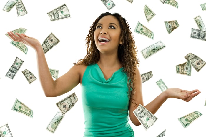 A smiling woman grabs hundred-dollar bills flying all around her.