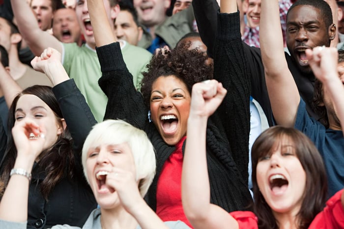 A crowd of people cheering with arms above their heads.