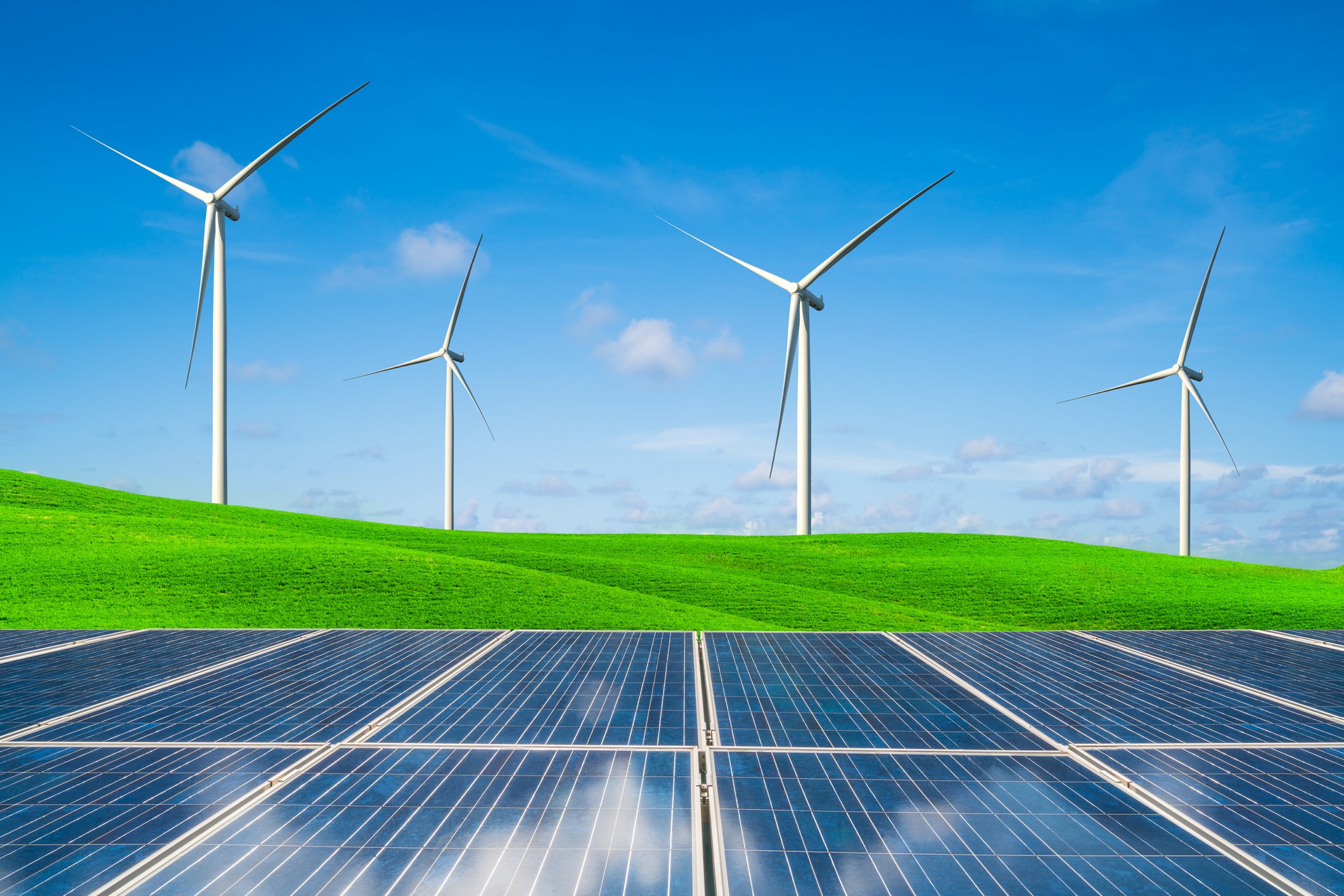 Solar panels in front of wind turbines on green grass