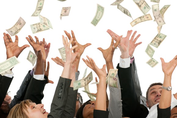 A group of people dressed in suit reaching for falling money.