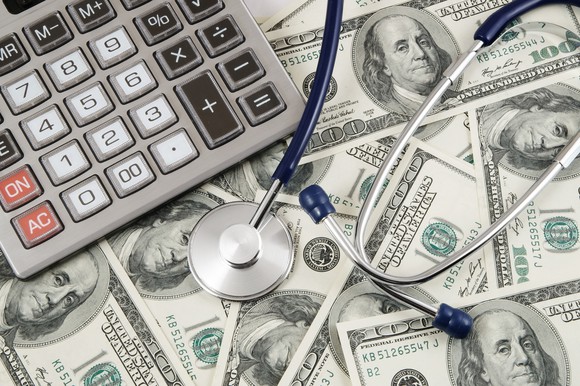 Cash spread across a surface with a stethoscope and calculator on top.
