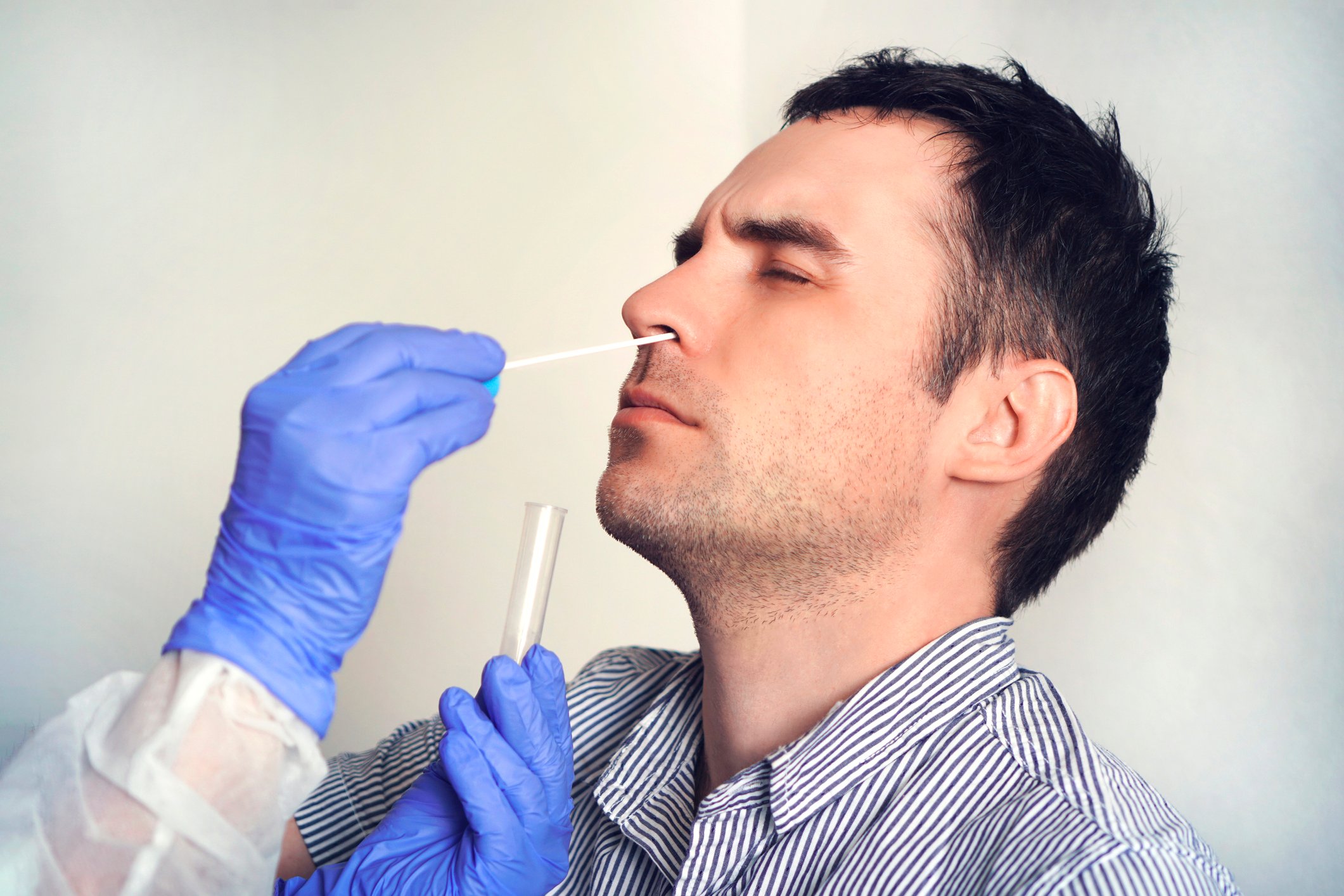 A man getting a nasal-swab test from a clinician wearing protective outerwear and gloves
