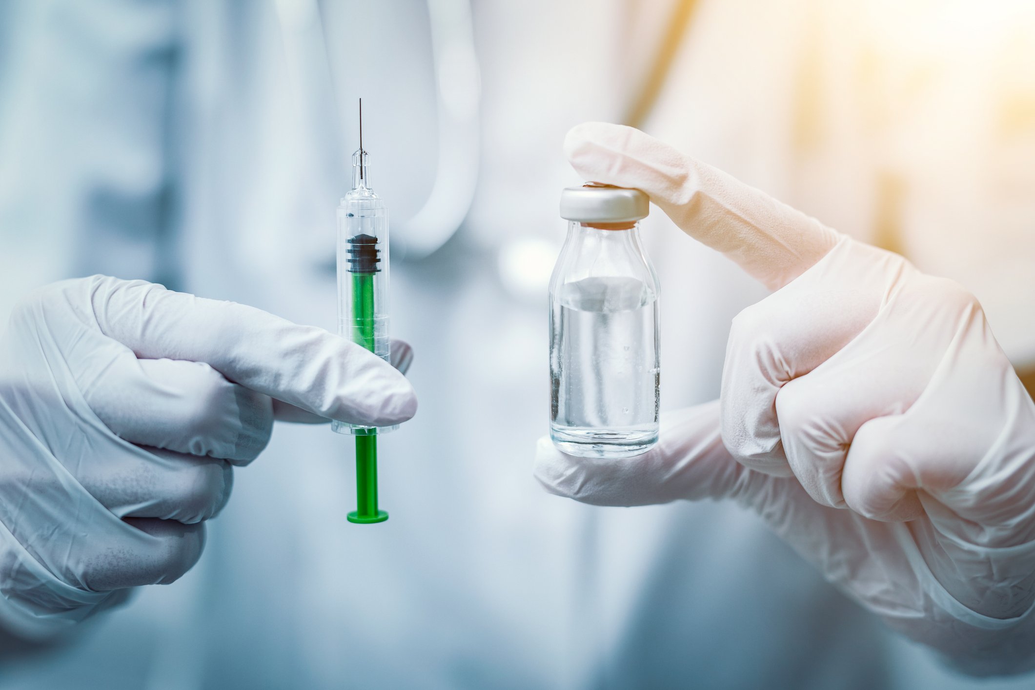 Gloved hands holding vial of medicine and a syringe.