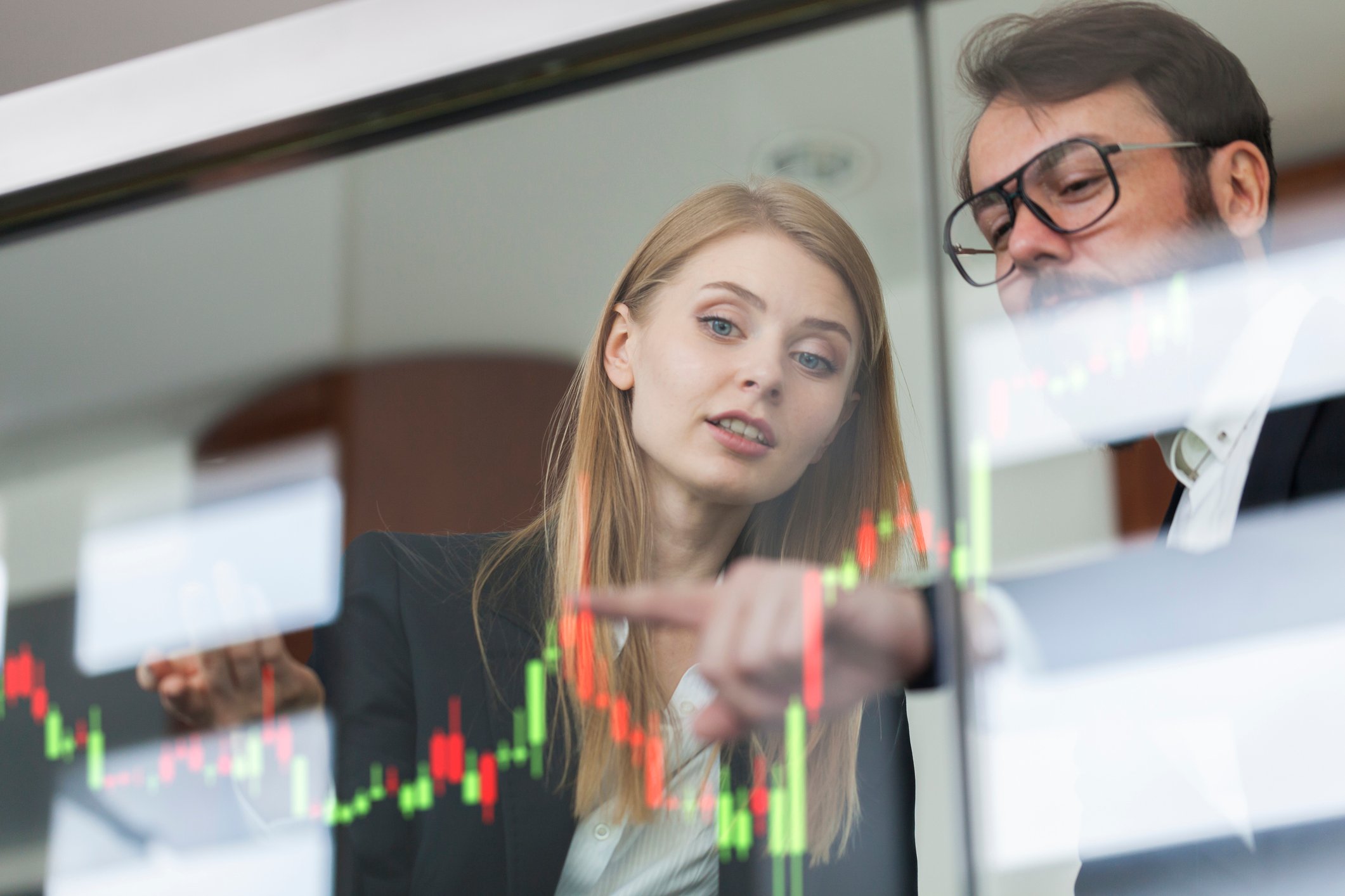 One trader points to a stock chart while another trader looks on.