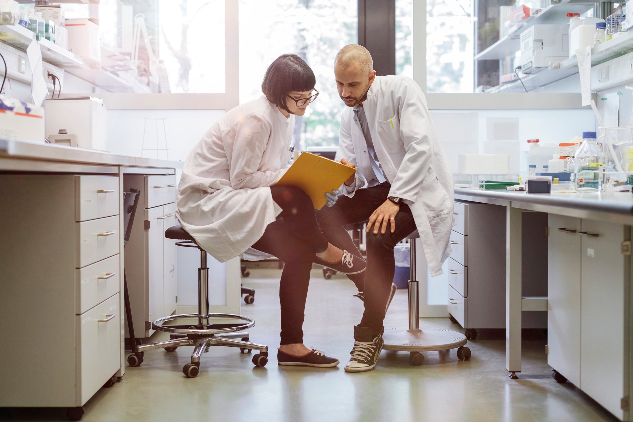 Two scientists consult document on a clipboard in a laboratory.