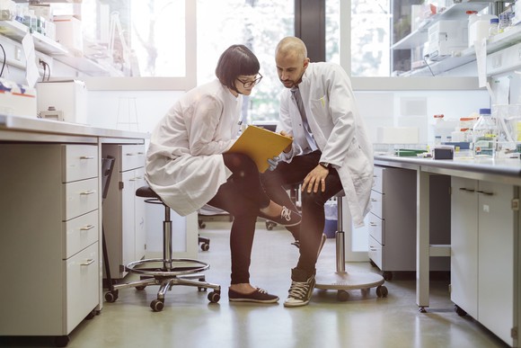 Two scientists consult document on a clipboard in a laboratory.