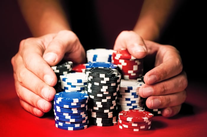 Two hands pushing big pile of poker chips forward on red felt.