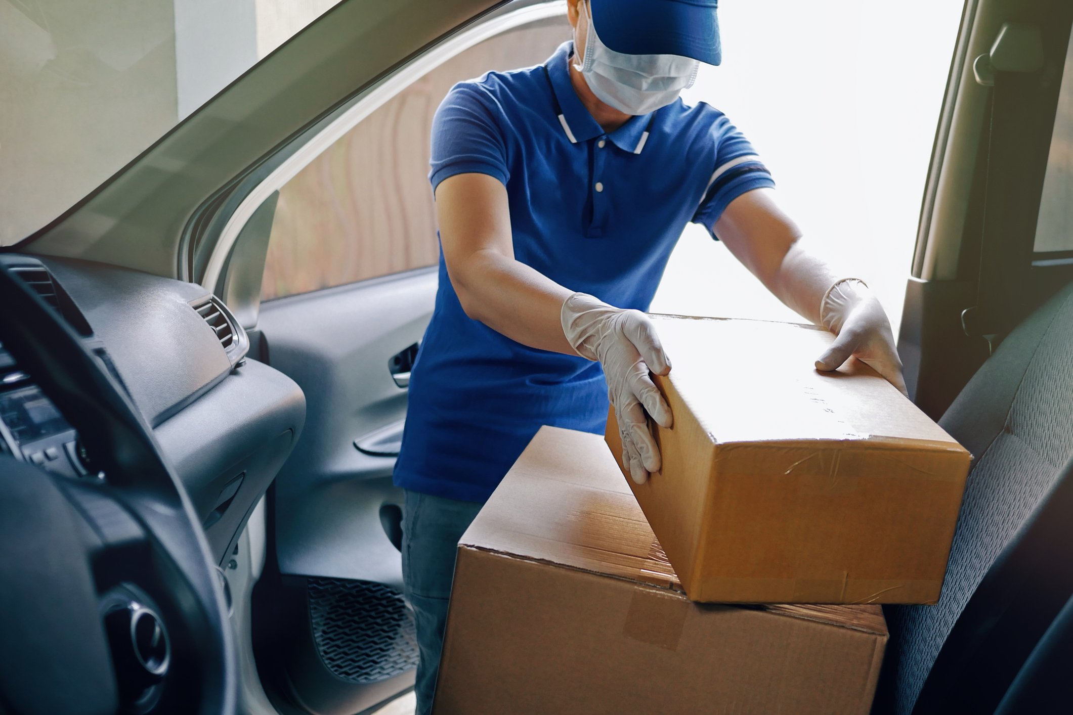 Delivery driver manipulating boxes in the driver's seat of a car.