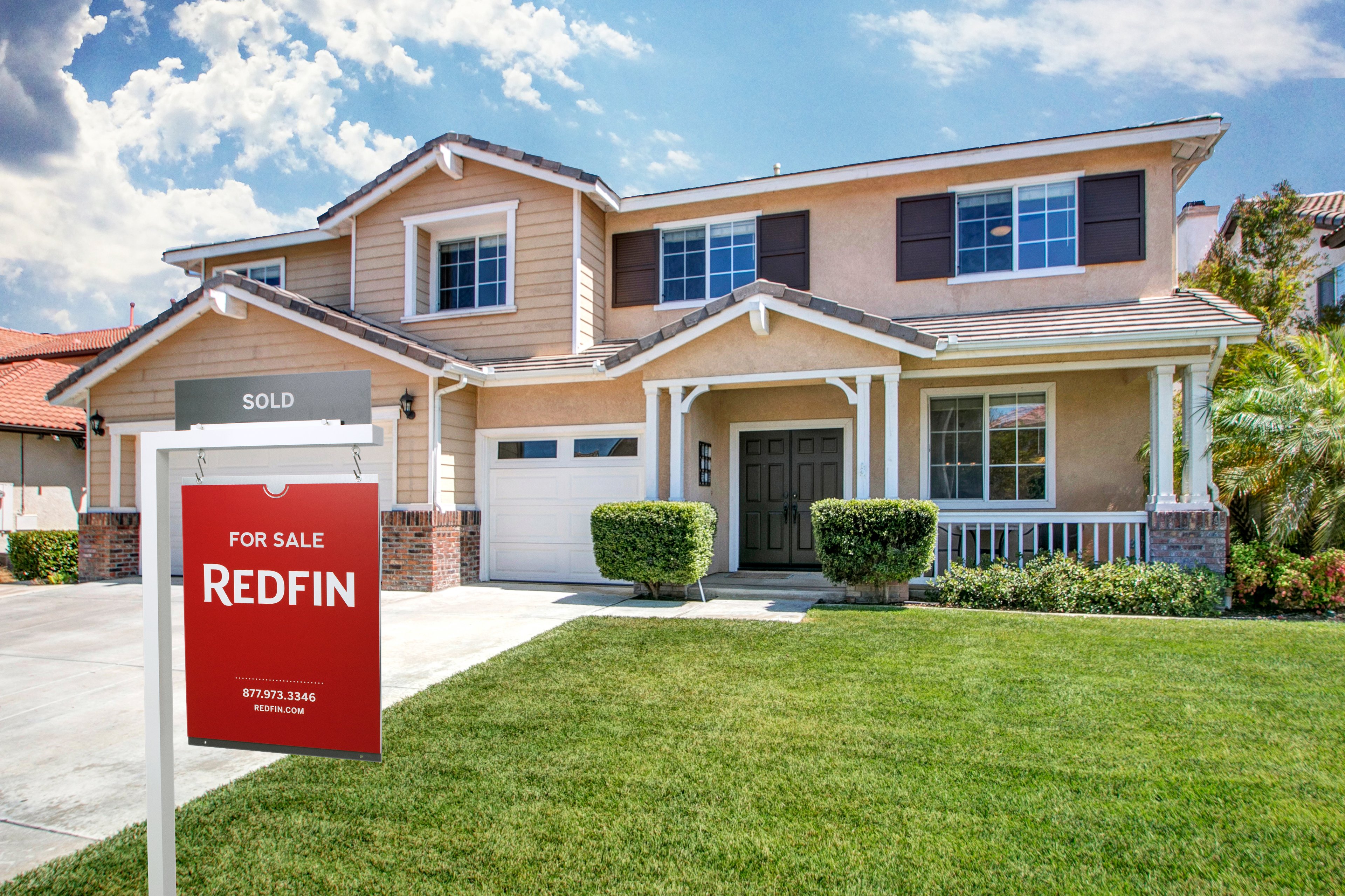 A Redfin for sale sign in front of a residential house. 