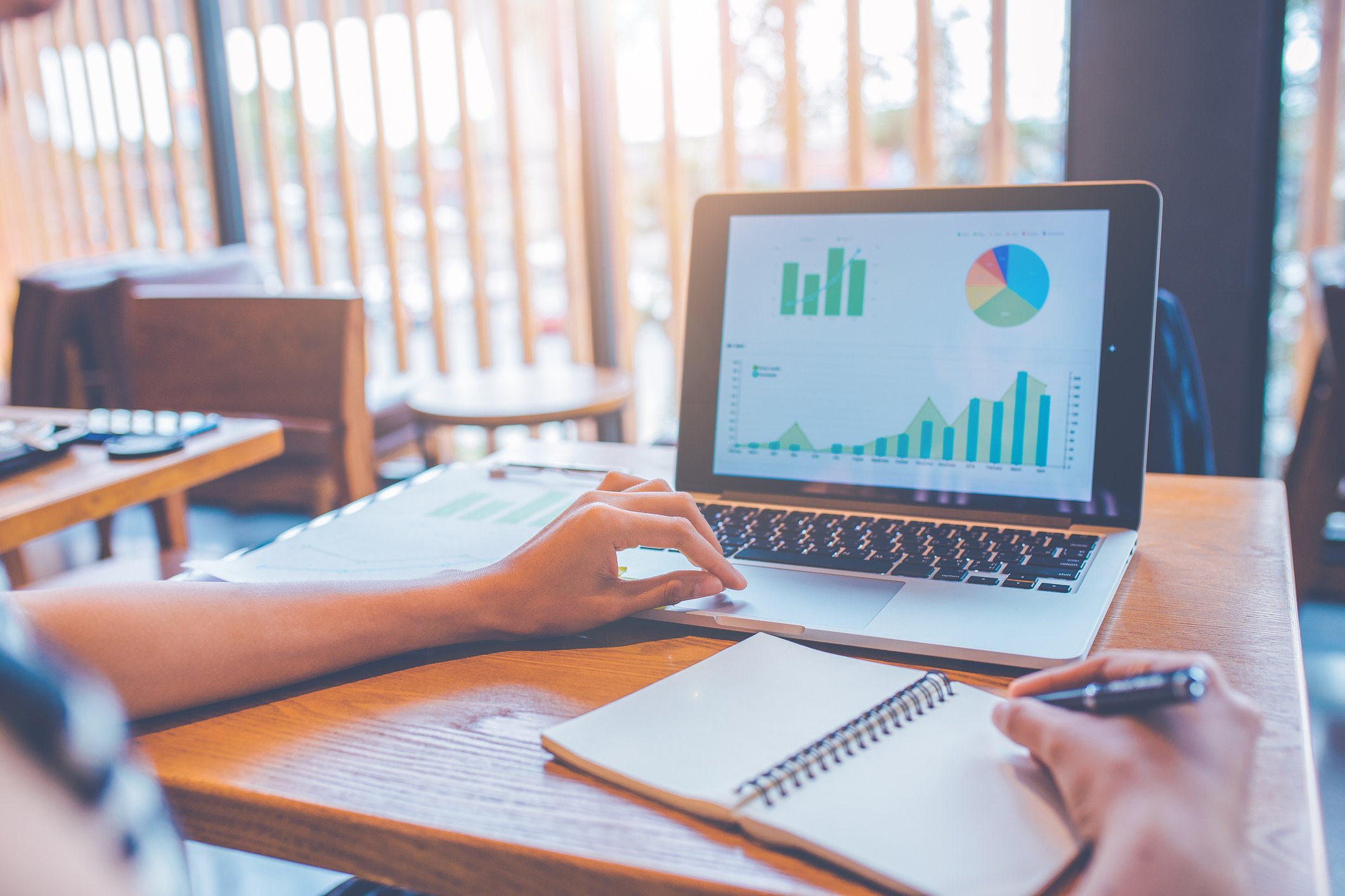 Investor looking at graph and bar charts on a laptop while using a notebook.