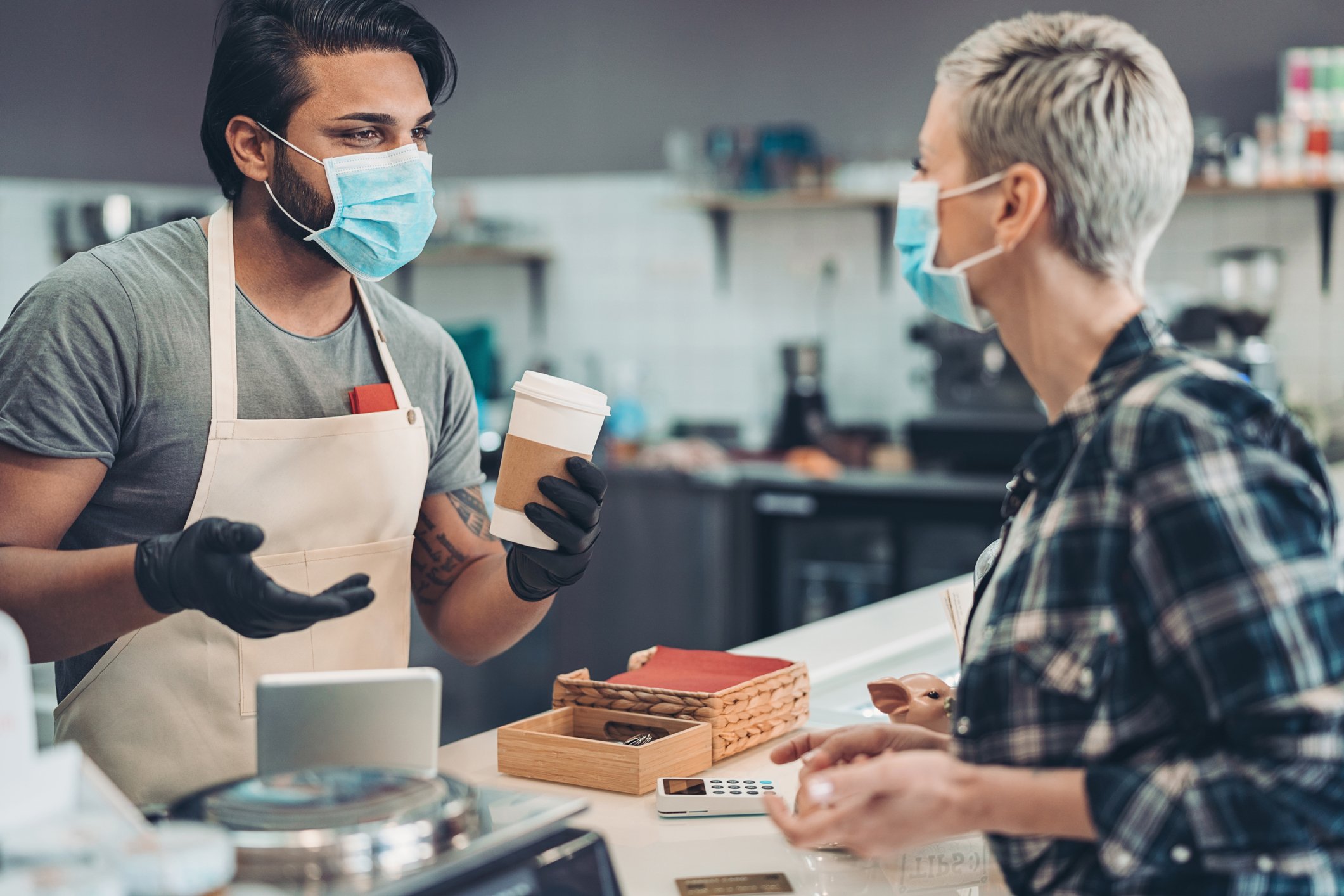 Masked barista handing cup of coffee to masked customer