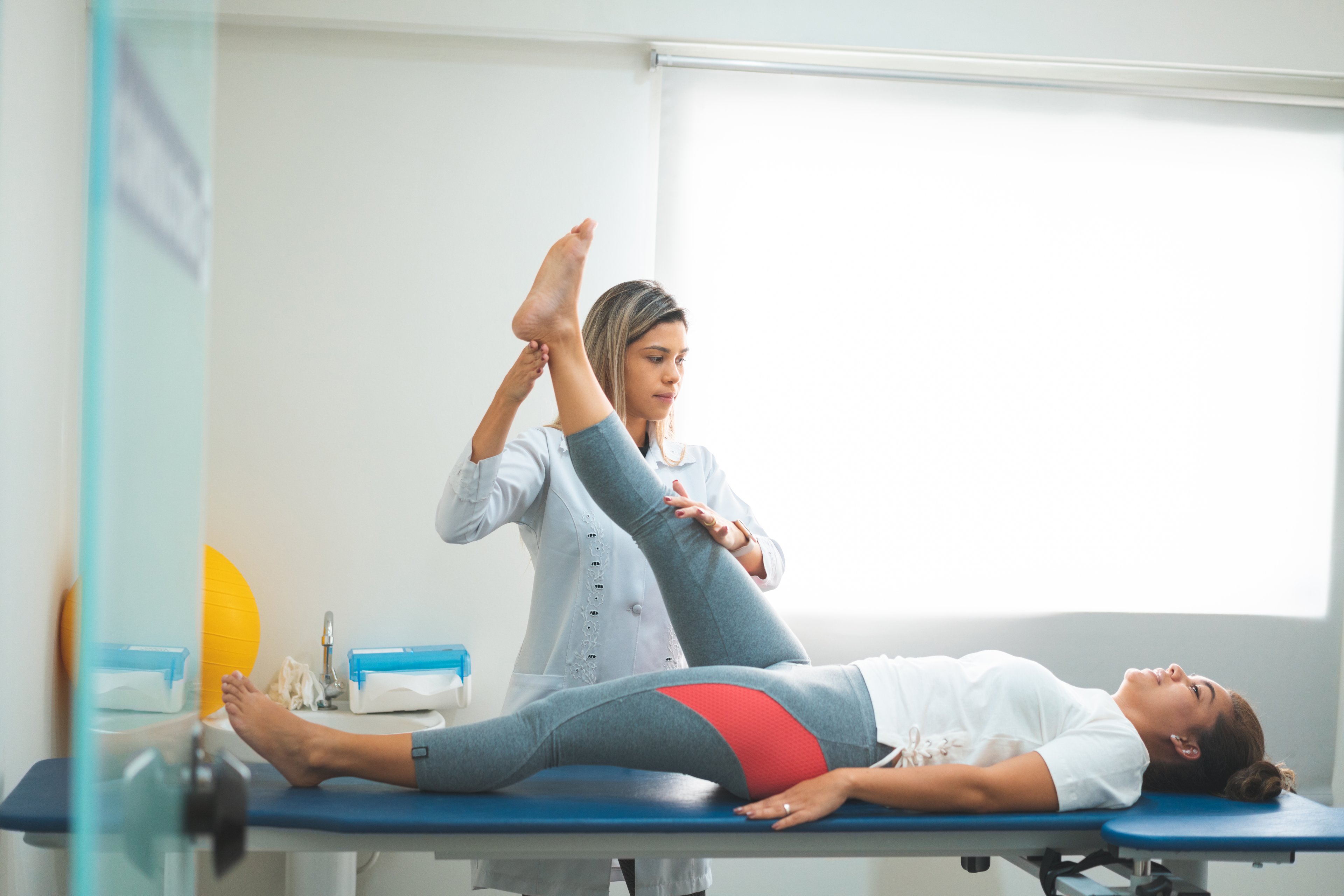 A female doctor works with a female patient lifting her leg.