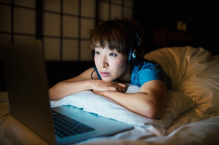 A young woman streams music into headphones while lying in bed.